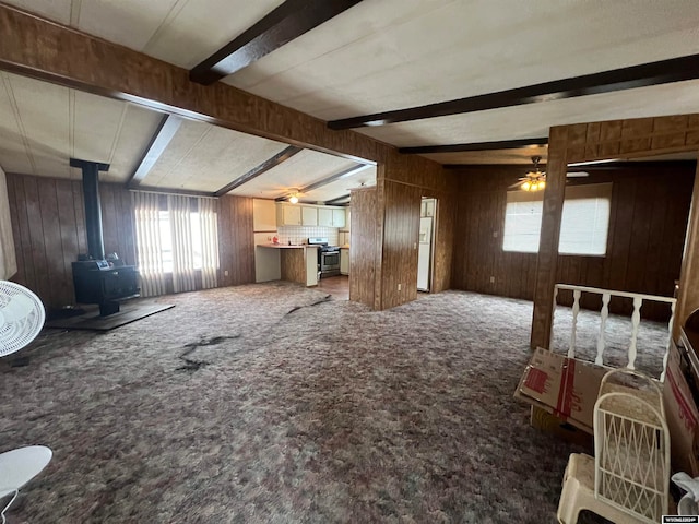 interior space featuring wood walls, beamed ceiling, a wood stove, and ceiling fan