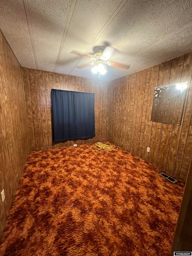 carpeted empty room featuring a textured ceiling, wooden walls, and ceiling fan