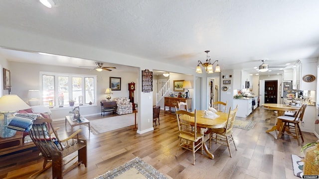 dining room featuring ceiling fan with notable chandelier, wood-type flooring, and a textured ceiling