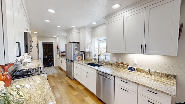 kitchen with stainless steel appliances, light hardwood / wood-style floors, sink, light stone countertops, and white cabinetry