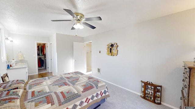 bedroom with a closet, a walk in closet, light carpet, sink, and ceiling fan