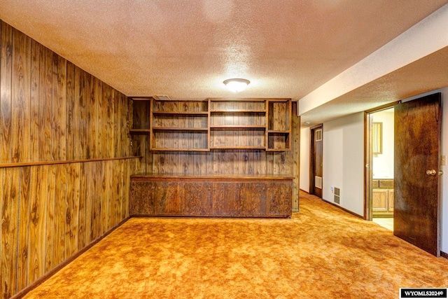 unfurnished living room featuring wood walls, a textured ceiling, and carpet flooring