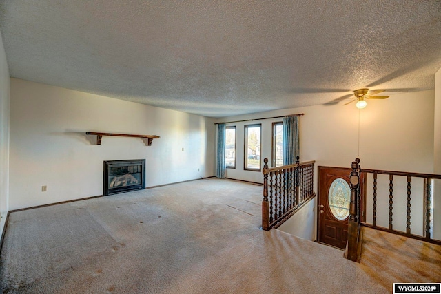 unfurnished living room with a textured ceiling, light colored carpet, and ceiling fan