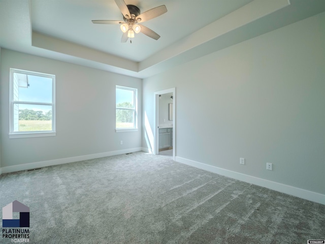 carpeted spare room featuring ceiling fan, baseboards, and a raised ceiling