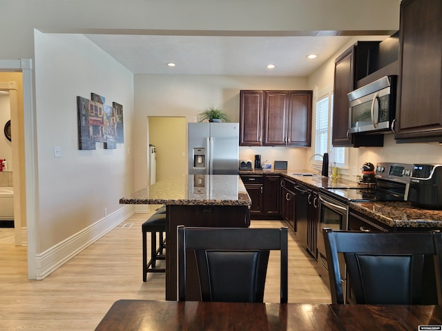 kitchen with light hardwood / wood-style floors, appliances with stainless steel finishes, dark stone counters, a kitchen bar, and a kitchen island