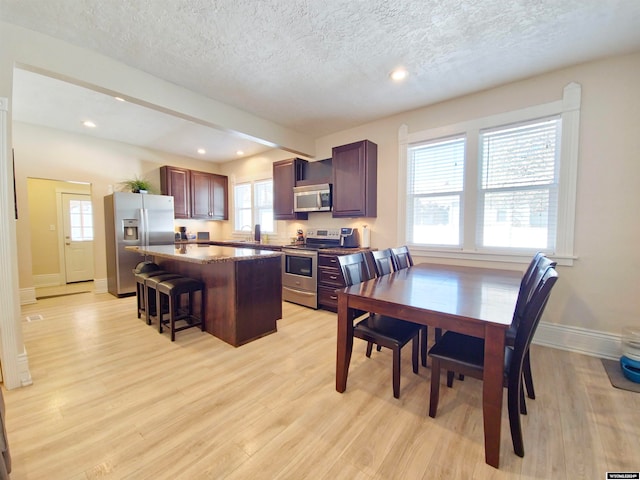 kitchen with appliances with stainless steel finishes, a textured ceiling, light hardwood / wood-style floors, a kitchen breakfast bar, and a center island