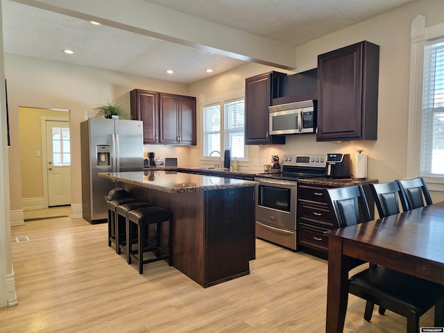 kitchen featuring stainless steel appliances, a kitchen island, a kitchen bar, beam ceiling, and light hardwood / wood-style floors