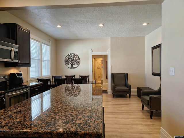 kitchen with appliances with stainless steel finishes, dark stone countertops, a textured ceiling, light hardwood / wood-style flooring, and a center island