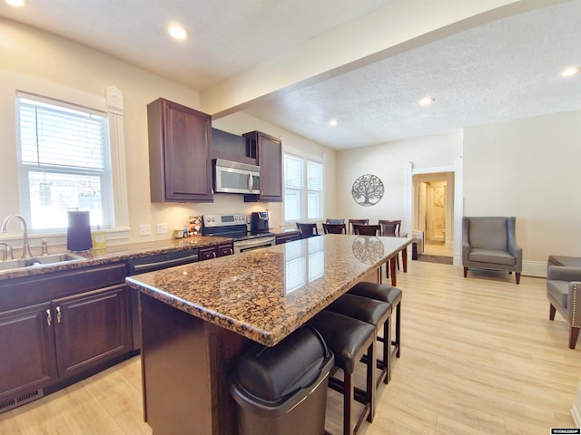 kitchen with stainless steel appliances, light wood-type flooring, sink, a breakfast bar, and a center island