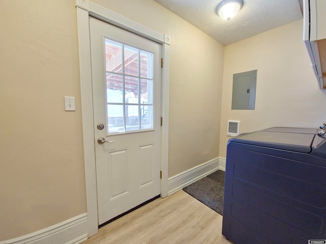 clothes washing area with electric panel, a textured ceiling, light hardwood / wood-style flooring, and washer / clothes dryer