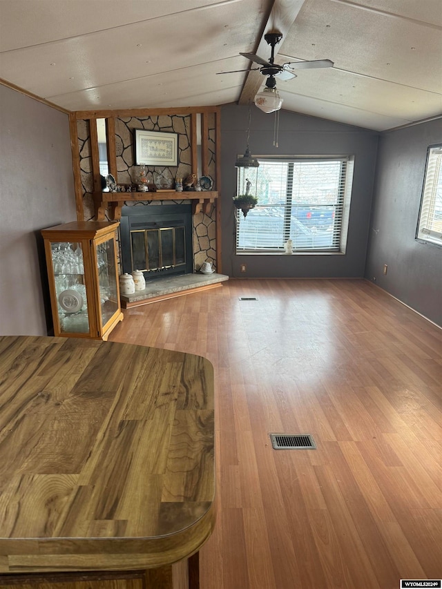 unfurnished living room with hardwood / wood-style floors, ceiling fan, vaulted ceiling, and a stone fireplace