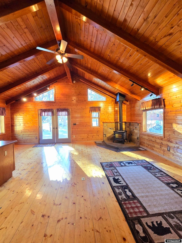 unfurnished living room featuring a wood stove, wood walls, wood ceiling, and light wood-type flooring