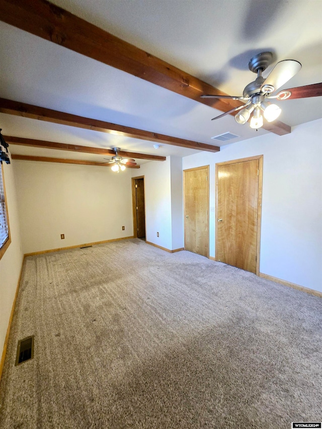 empty room featuring carpet, ceiling fan, and beamed ceiling