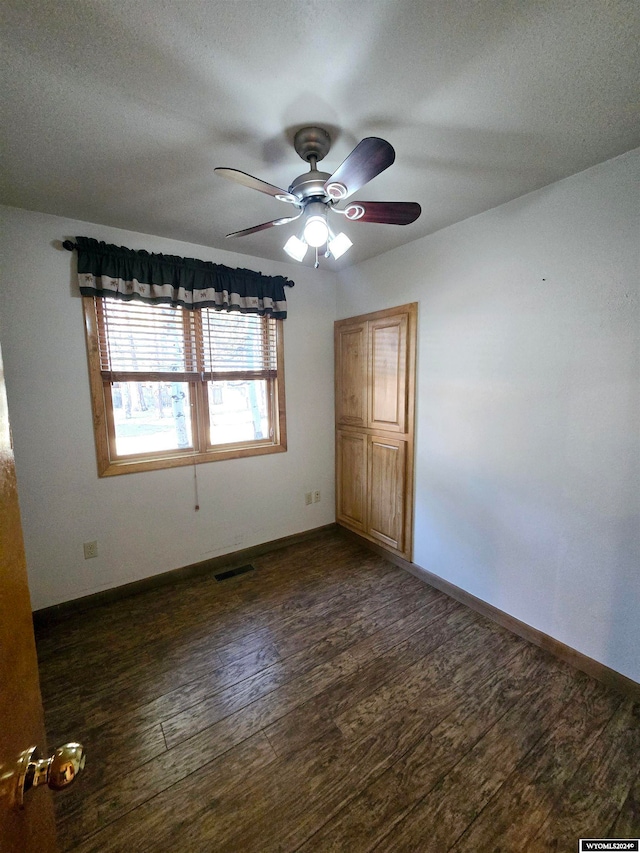 spare room with a textured ceiling, ceiling fan, and dark wood-type flooring