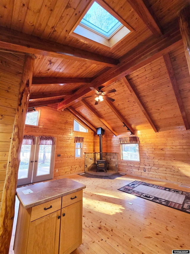 interior space featuring a wood stove, lofted ceiling with skylight, wooden walls, and light hardwood / wood-style floors