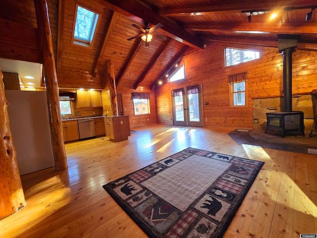 living room featuring beam ceiling, a wood stove, ceiling fan, wood walls, and light wood-type flooring