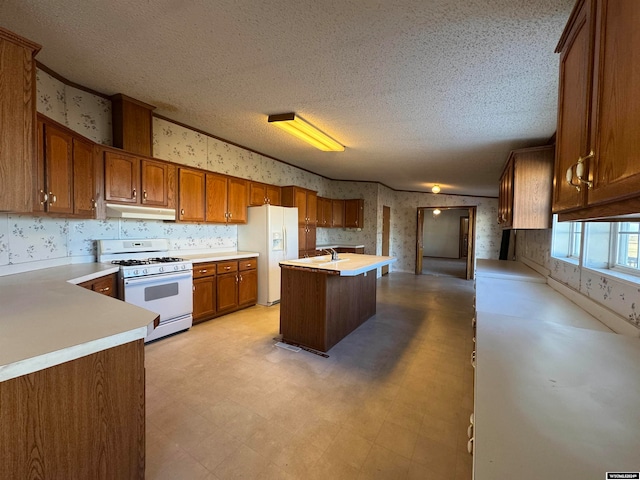 kitchen with a textured ceiling, sink, white appliances, and a kitchen island with sink