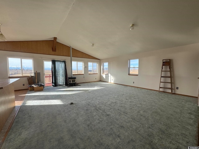 unfurnished living room with carpet flooring, vaulted ceiling, a wood stove, and plenty of natural light