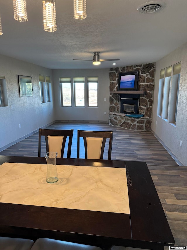 dining room with hardwood / wood-style flooring, ceiling fan, a stone fireplace, and a textured ceiling