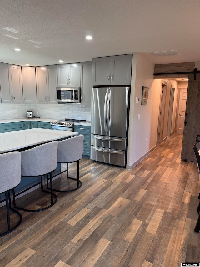 kitchen with dark hardwood / wood-style floors, gray cabinets, a barn door, appliances with stainless steel finishes, and tasteful backsplash