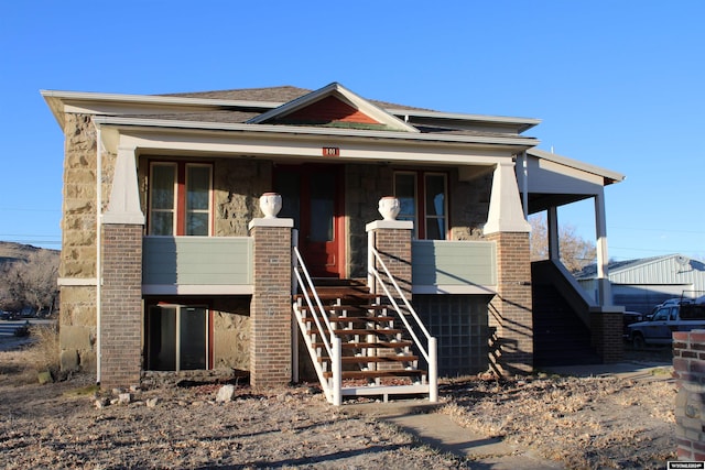view of front facade featuring a porch, brick siding, and stairs