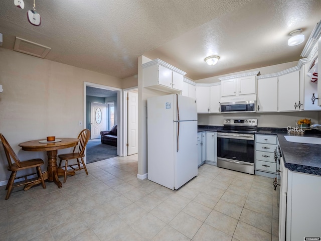 kitchen featuring dark countertops, stainless steel appliances, a textured ceiling, white cabinetry, and a sink