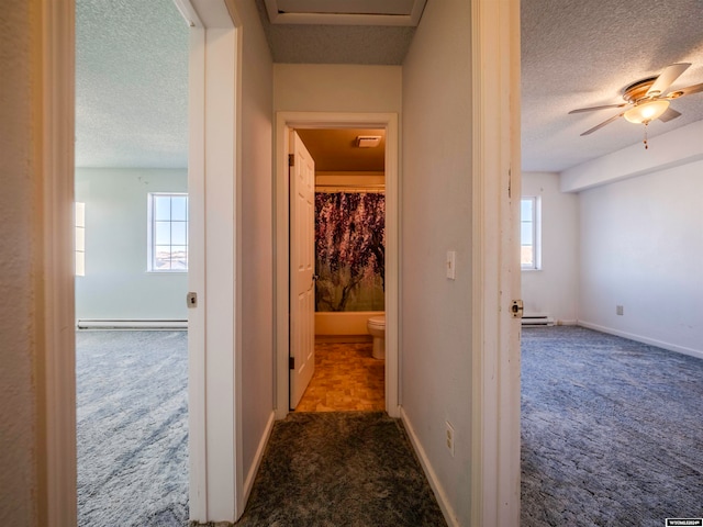 corridor featuring a baseboard heating unit, carpet flooring, baseboards, and a textured ceiling