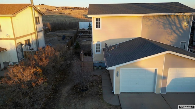 view of side of property with concrete driveway, a garage, and fence