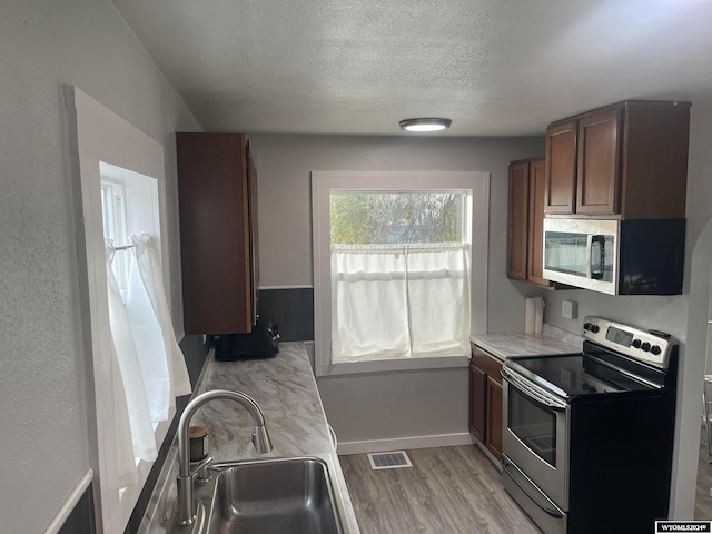 kitchen featuring a textured ceiling, stainless steel appliances, light hardwood / wood-style flooring, and sink