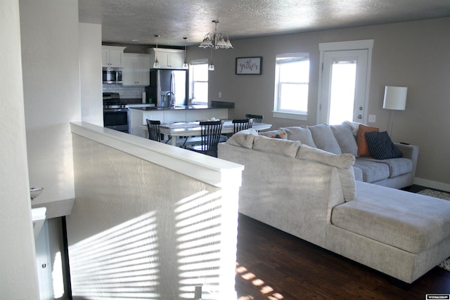 living room with a notable chandelier, dark hardwood / wood-style floors, sink, and a textured ceiling