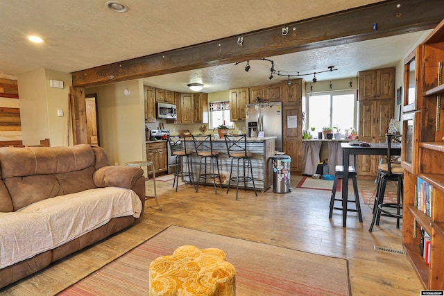 living room with beamed ceiling, light wood-type flooring, and a textured ceiling