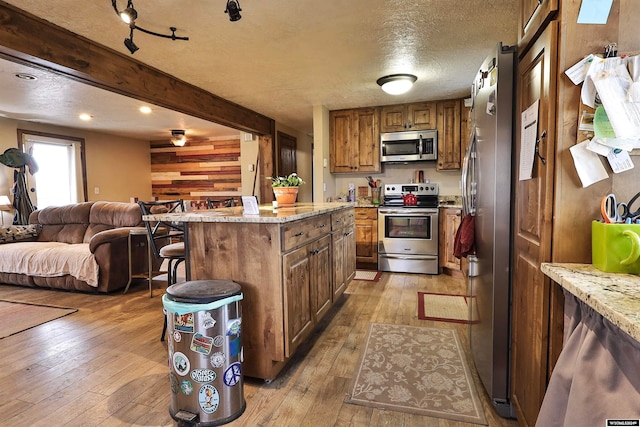 kitchen featuring light stone countertops, light hardwood / wood-style floors, a textured ceiling, a kitchen island, and appliances with stainless steel finishes