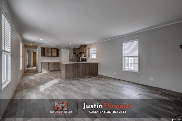 kitchen with stainless steel fridge, light wood-type flooring, a textured ceiling, ornamental molding, and kitchen peninsula