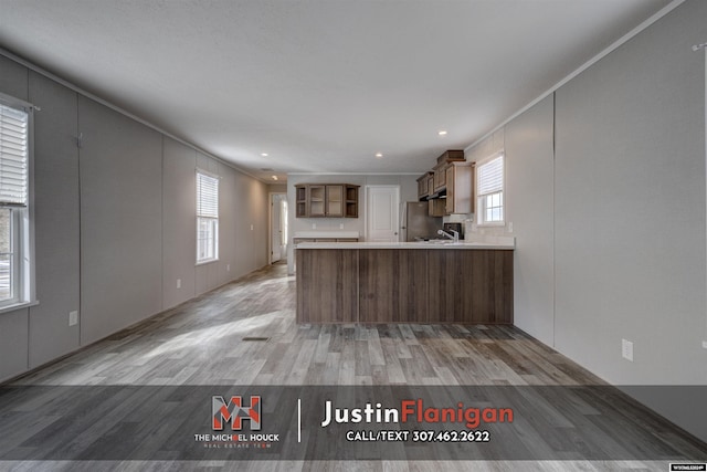 kitchen featuring stainless steel refrigerator, kitchen peninsula, a healthy amount of sunlight, and light hardwood / wood-style floors