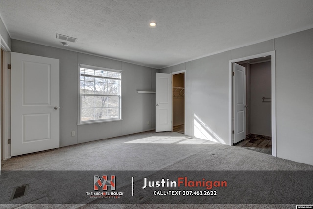 unfurnished bedroom featuring carpet flooring, a textured ceiling, a spacious closet, and a closet