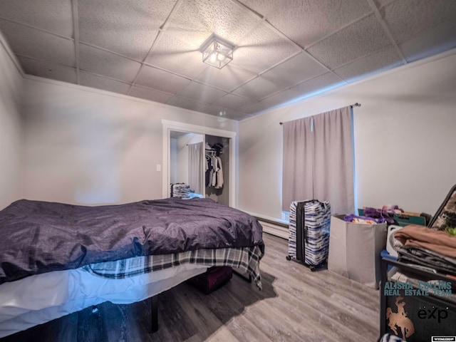 bedroom with baseboard heating, a closet, hardwood / wood-style floors, and a drop ceiling