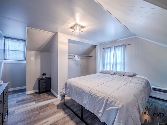 bedroom with vaulted ceiling, light hardwood / wood-style flooring, wooden walls, and a closet