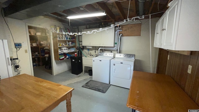 clothes washing area with wood walls, sink, cabinets, and independent washer and dryer