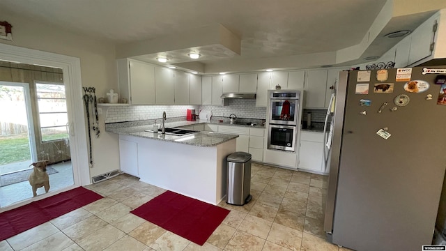 kitchen featuring kitchen peninsula, decorative backsplash, stainless steel appliances, sink, and white cabinetry