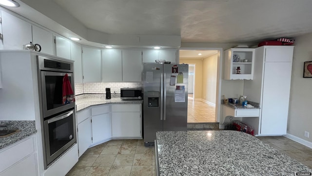 kitchen with white cabinetry, tasteful backsplash, light stone counters, light tile patterned flooring, and appliances with stainless steel finishes