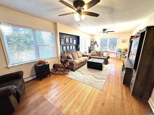 living room featuring ceiling fan, light hardwood / wood-style floors, a textured ceiling, and a baseboard heating unit