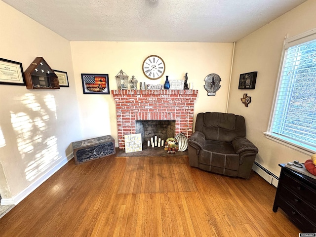 living room with a wealth of natural light, light hardwood / wood-style flooring, a baseboard heating unit, and a brick fireplace