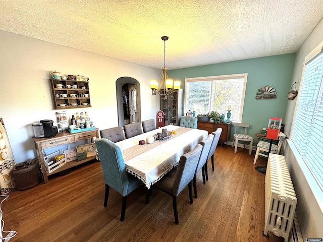 dining area featuring a chandelier, radiator heating unit, dark wood-type flooring, and a textured ceiling