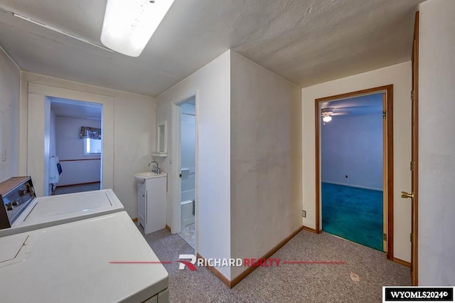 clothes washing area featuring washing machine and clothes dryer, light colored carpet, ceiling fan, and sink