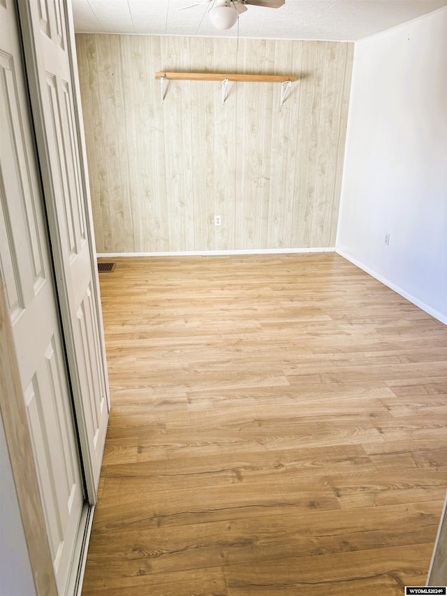 empty room featuring light wood-type flooring, ceiling fan, and wood walls