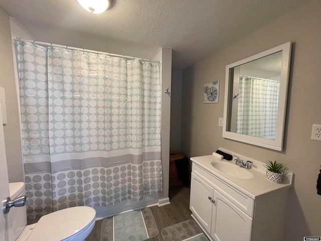 full bathroom with hardwood / wood-style floors, vanity, shower / bath combination with curtain, toilet, and a textured ceiling