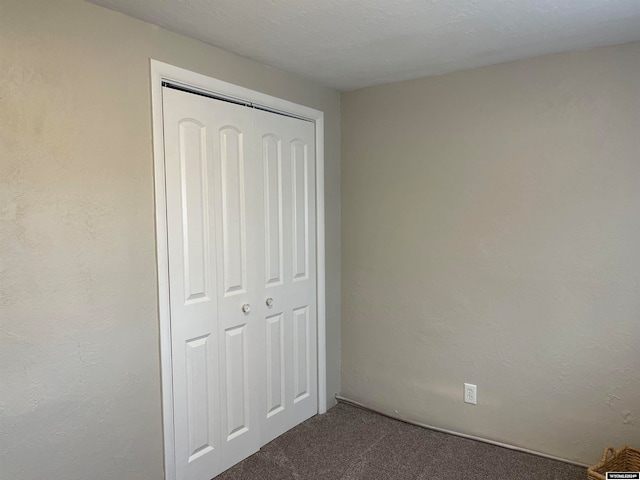 unfurnished bedroom with a closet, dark carpet, and a textured ceiling