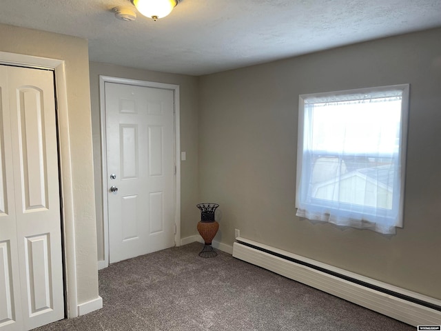 empty room featuring carpet flooring, a textured ceiling, and a baseboard heating unit