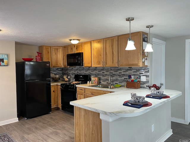 kitchen featuring sink, kitchen peninsula, decorative backsplash, black appliances, and hardwood / wood-style flooring