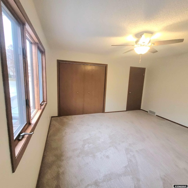 unfurnished bedroom featuring ceiling fan, a closet, carpet floors, and a textured ceiling